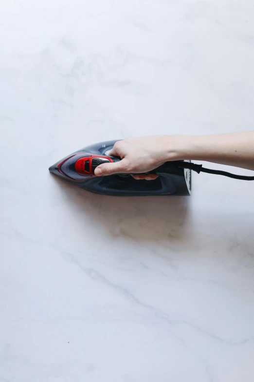 a person using a steam iron on a table, on a large marble wall, black steel with red trim, jen atkin, tutorial
