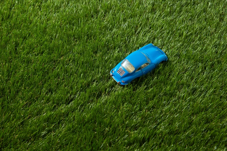 a toy car sitting on top of a lush green field, inspired by Chris LaBrooy, conceptual art, shot on hasselblad, blue grass, porsche 356, grass texture