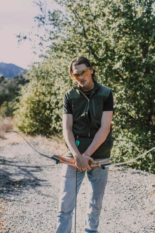 a man standing on top of a gravel road, holding a bow and arrow, jamie campbell bower, profile image, bay area