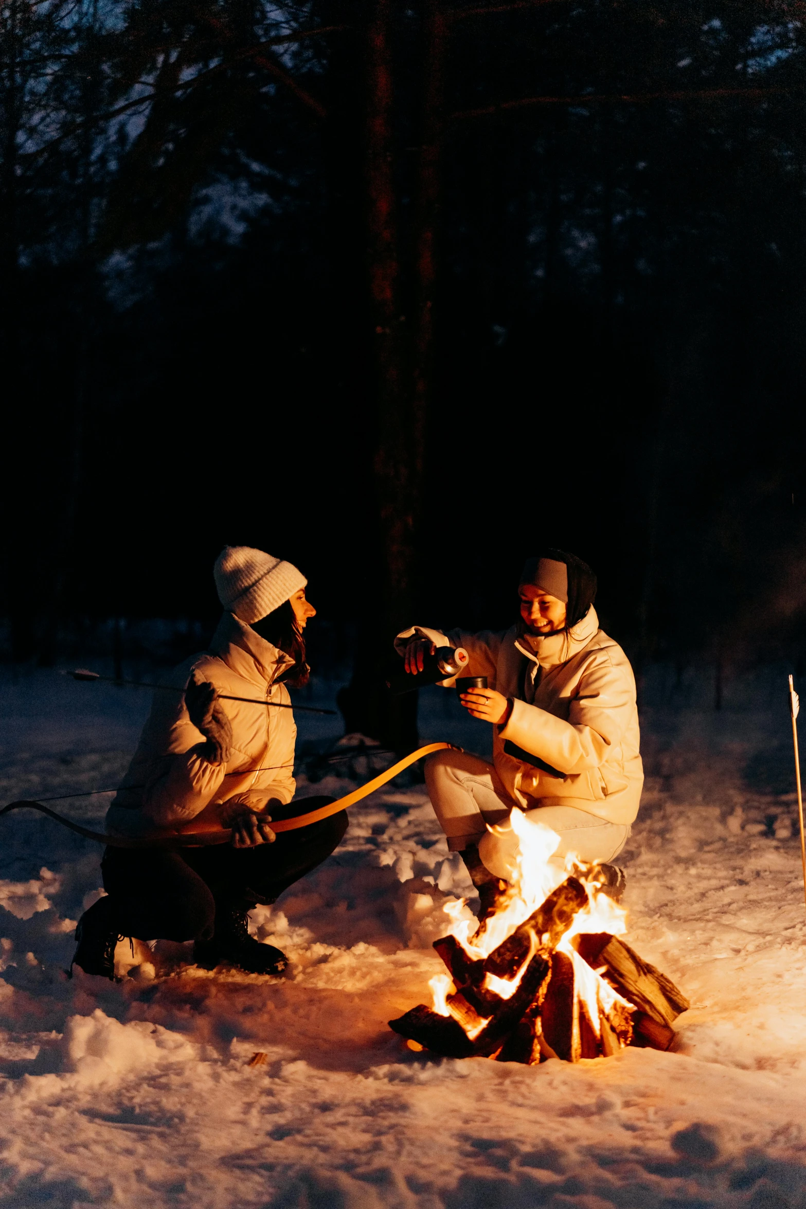 two people sitting around a campfire in the snow, inspired by Einar Hakonarson, holding a torch, drink, candid shot