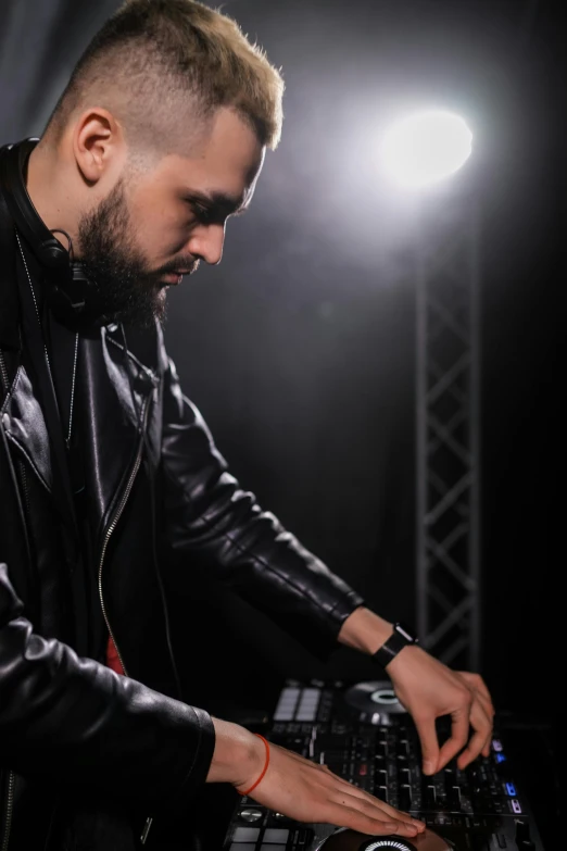 a man in a leather jacket mixing music on a mixer, inspired by Ottó Baditz, trending on pexels, with a beard and a black shirt, profile pose, dasha taran, club lighting