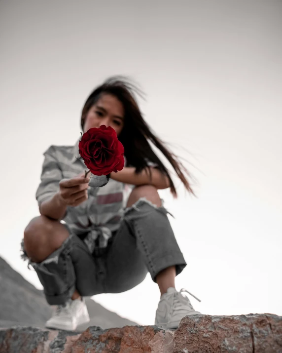 a woman sitting on a rock holding a rose, by Robbie Trevino, pexels contest winner, red and grey only, asian human, lgbtq, snapchat photo