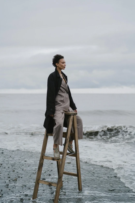 a man sitting on a ladder on the beach, a portrait, by Christen Dalsgaard, pexels, renaissance, she is wearing a wet coat, wearing wool suit, jovana rikalo, sitting on a mocha-colored table