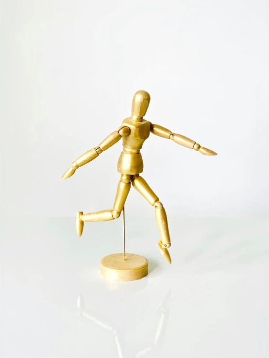 a wooden mannequin standing on a white surface, dancing a jig, accented in bright metallic gold, fully posable, 2019 trending photo