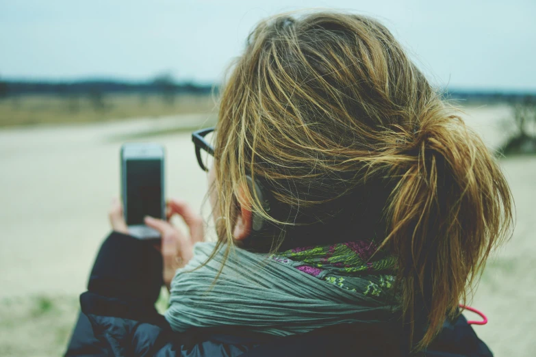 a woman taking a picture with her cell phone, a picture, trending on pexels, windy hair, with glasses, with back to the camera, grainy