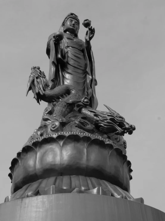 a black and white photo of a statue on top of a building, a statue, by Shen Quan, sōsaku hanga, sitting on a lotus flower, shenron, closeup of arms, centred in image