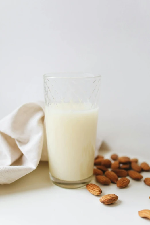 a glass of almond milk next to some almonds, by Nicolette Macnamara, soft white glow, glassware, chiffon, 6 pack