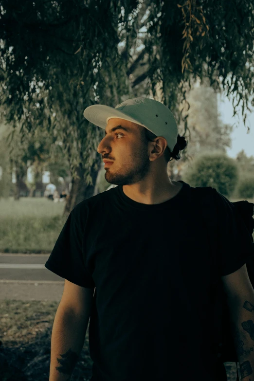 a man standing under a tree with a skateboard, an album cover, pexels contest winner, headshot profile picture, wearing a backwards baseball cap, elias chatzoudis, low - lighting