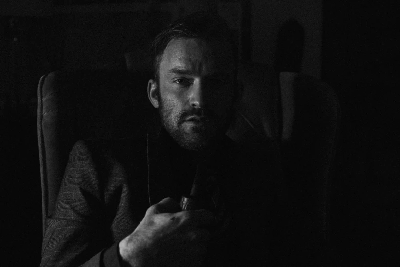 a black and white photo of a man sitting in a chair, a black and white photo, unsplash, charlie cox, gloomy lighting!!!, a man wearing a black jacket, gif