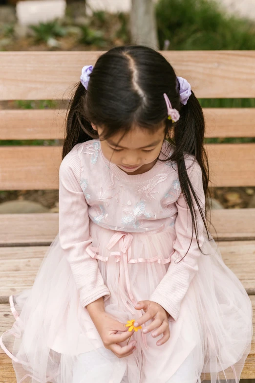 a little girl sitting on top of a wooden bench, inspired by Kate Greenaway, pexels contest winner, pink dress, touching heads, young asian girl, little