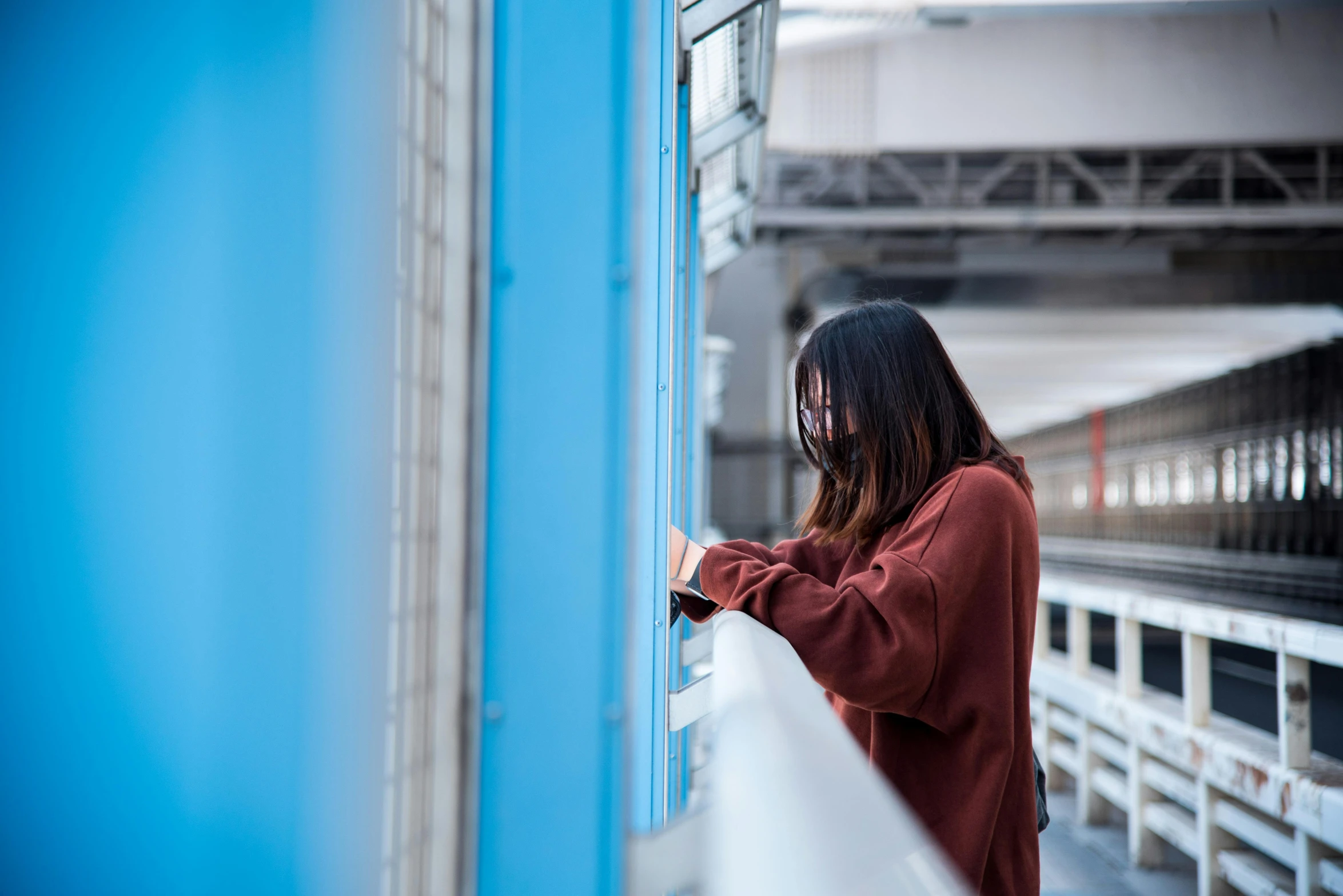 a woman standing on a bridge looking at her cell phone, by Julia Pishtar, pexels contest winner, graffiti, brown and cyan blue color scheme, monorail station, looking through a window frame, a young asian woman