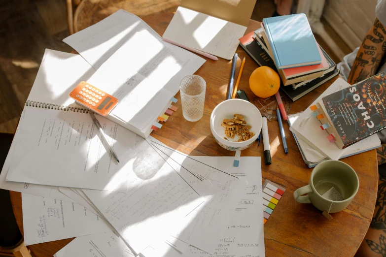 a wooden table topped with lots of papers and a cup of coffee, a drawing, process art, textbooks and books, thumbnail, whiteboards, sun lighting