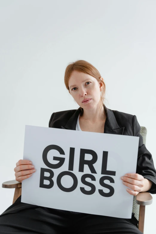 a woman sitting in a chair holding a sign, trending on unsplash, girlboss, wearing headmistress uniform, a redheaded young woman, guilt