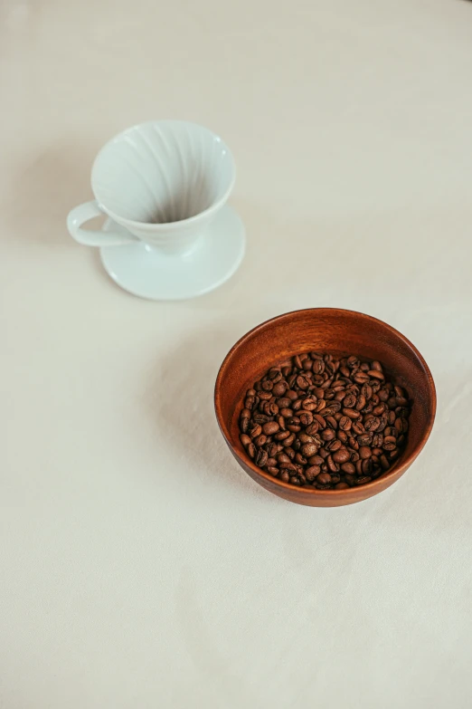 a bowl of coffee beans next to a cup of coffee, detailed product image, medium-shot, curated collection, at home