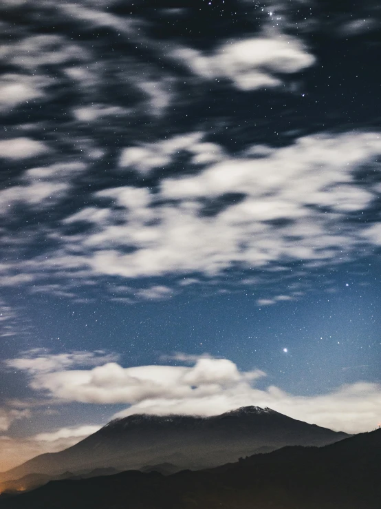 a night sky with clouds and a mountain in the background, looking towards camera, scattered clouds