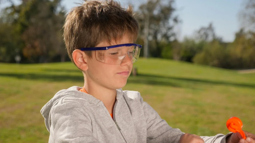 a young boy in glasses holding a pair of scissors, sleek blue visor for eyes, al fresco, scientific glassware, shot with canon eoa 6 d mark ii