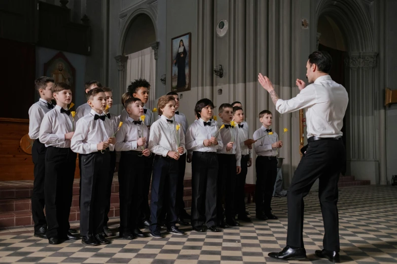 a man standing in front of a group of children, an album cover, by László Balogh, pexels, antipodeans, in a large cathedral, actors, boys, performing