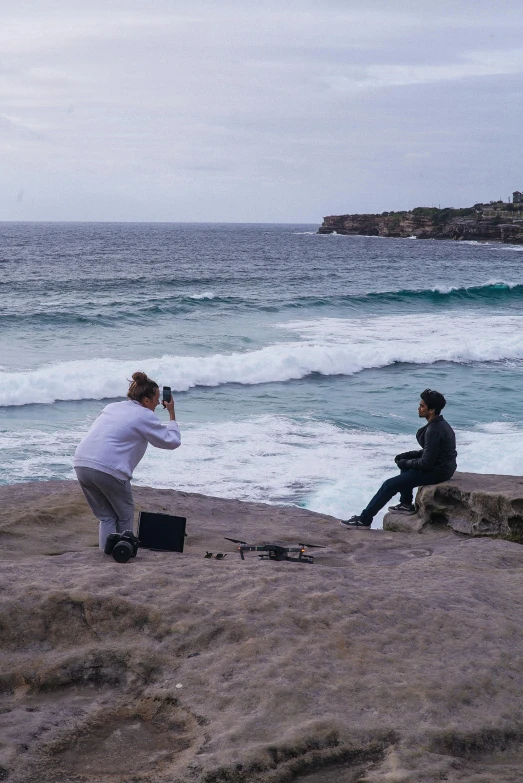 a couple of people sitting on top of a rock next to the ocean, holding a camera, sydney, slide show, harsh flash photo