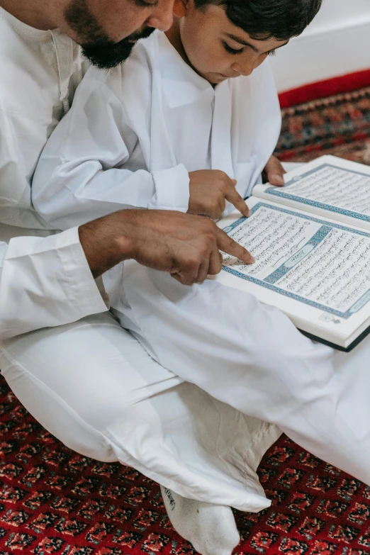 a man and a boy sitting on the floor reading a book, hurufiyya, wearing white robes, professional image, islamic, charts