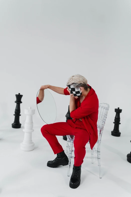 a man sitting on a chair surrounded by chess pieces, inspired by Anna Füssli, trending on pexels, video art, red jumpsuit, with a mirror, red hat, cai xukun