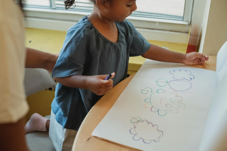 a little girl is drawing on a piece of paper, a child's drawing, by Arabella Rankin, pexels contest winner, whiteboards, dot painting, full figure, papers on table