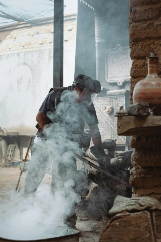 a man that is standing in front of a pot, blowing smoke, woodfired, damascus, working hard