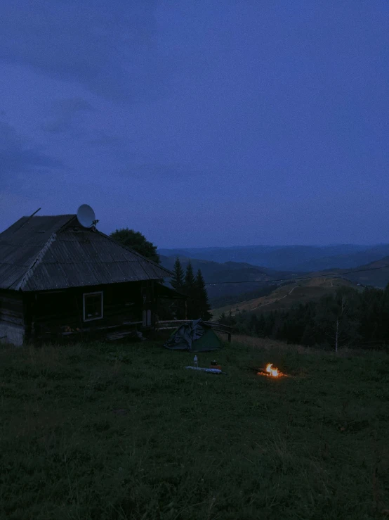 a small cabin sitting on top of a lush green hillside, by Attila Meszlenyi, at a campfire at night, ukraine. photography, ☁🌪🌙👩🏾, profile image