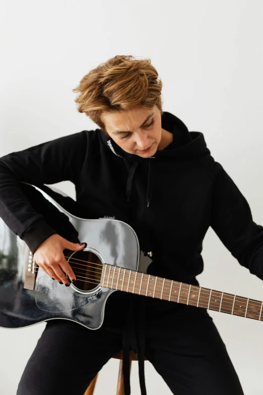 a woman sitting on a stool playing a guitar, pexels contest winner, antipodeans, wearing a black hoodie, caspar david, profile image, androgynous male