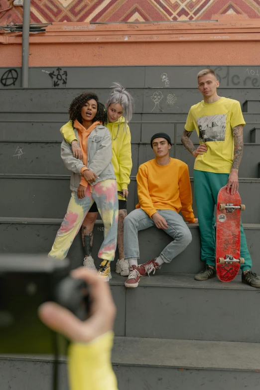 a man taking a picture of a group of skateboarders, trending on pexels, yellow clothes, non binary model, promo image, grey orange