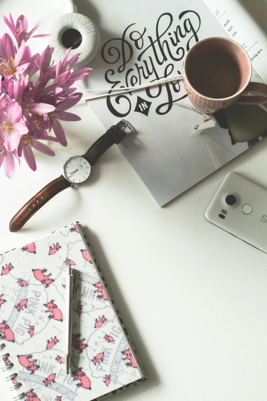 a cup of coffee sitting on top of a table next to a cell phone, floral patterned skin, wearing a watch, flatlay book collection, sitting at a desk