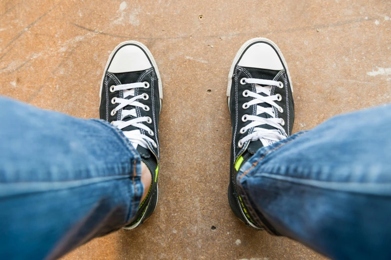 a pair of black sneakers sitting on top of a cement floor, by Carey Morris, trending on pexels, ( ( ( wearing jeans ) ) ), standing in a church, acid-green sneakers, converse