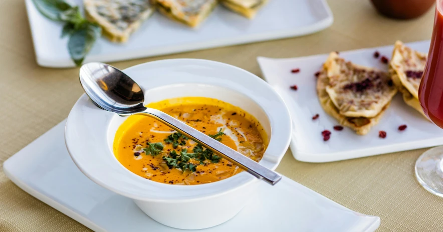 a bowl of soup sitting on top of a white plate, inspired by Géza Dósa, pexels, hurufiyya, ocher and turquoise colors, restaurant menu photo, middle eastern, orange gi