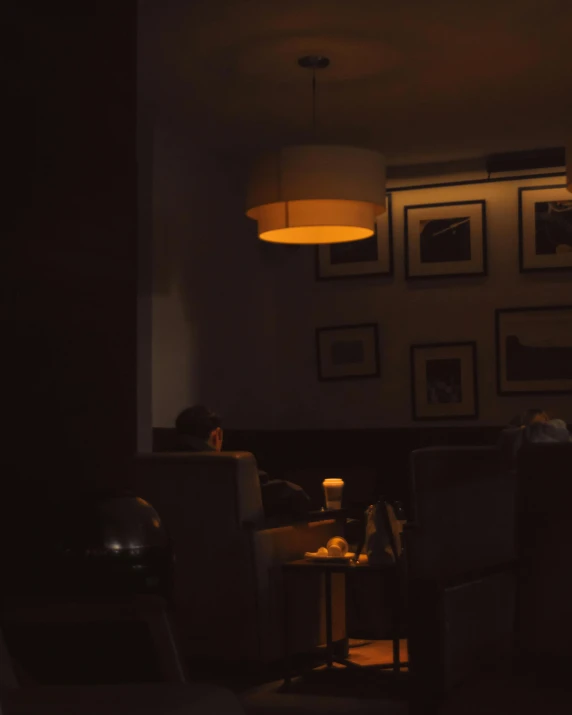 a person sitting at a table in a dark room, cafe lighting, two buddies sitting in a room, muted lights, low quality photo