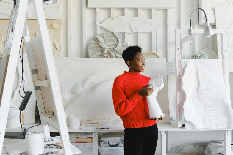 a woman standing in a room holding a piece of paper, by Lucette Barker, pexels contest winner, process art, wearing a red turtleneck sweater, kara walker james jean, in a white boho style studio, architectural painting