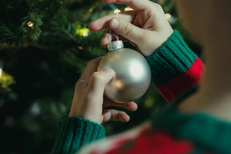 a person holding a silver ornament in front of a christmas tree, pexels contest winner, arts and crafts movement, teenage girl, early evening, behind the scenes, some spherical