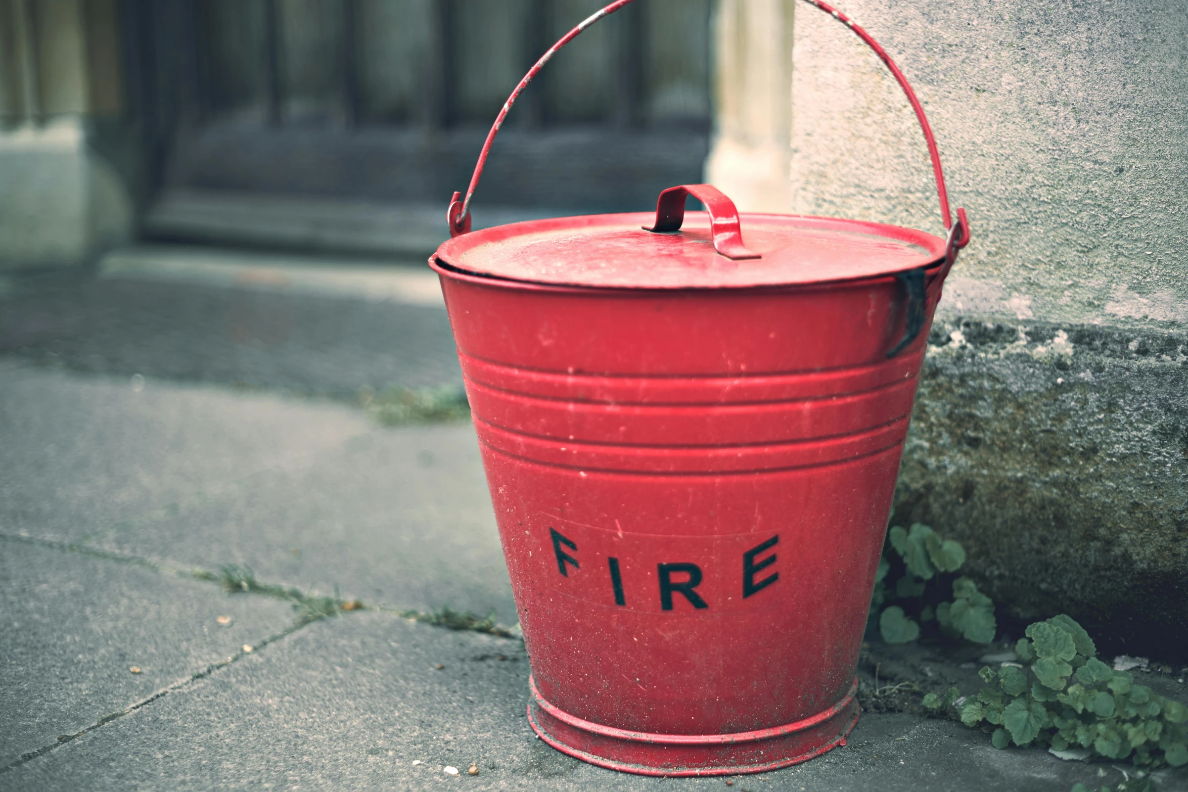 a red fire bucket sitting on the side of a building, pexels, instagram picture, vintage photo, grey, small