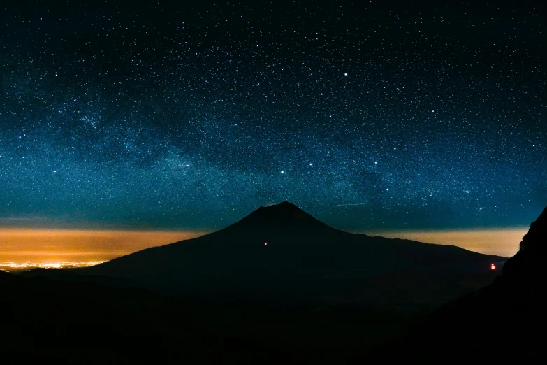 a person standing on top of a mountain under a night sky, pexels contest winner, magical realism, volcano in background, stars and paisley filled sky, panorama view of the sky, night time footage