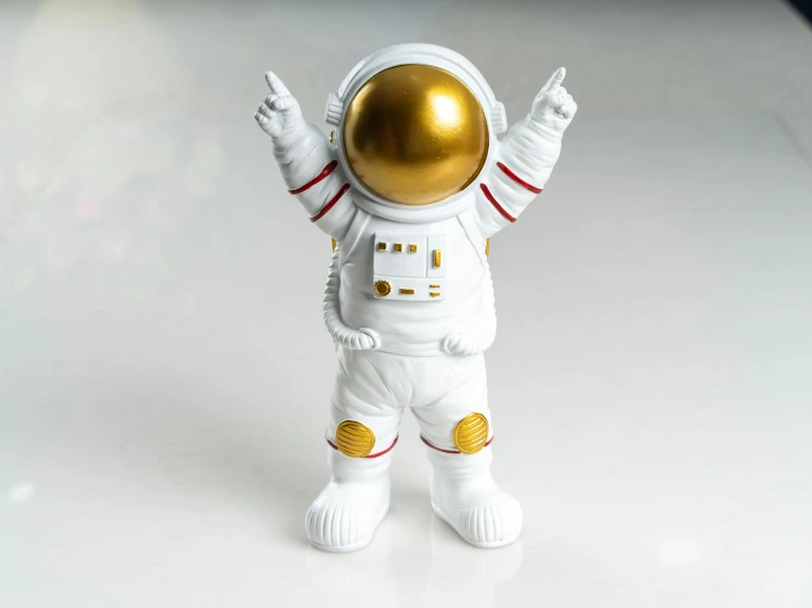 a close up of an astronaut figurine on a table, inspired by Jeff Koons, pexels contest winner, waving at the camera, on a white background, golden detailing, made out of plastic