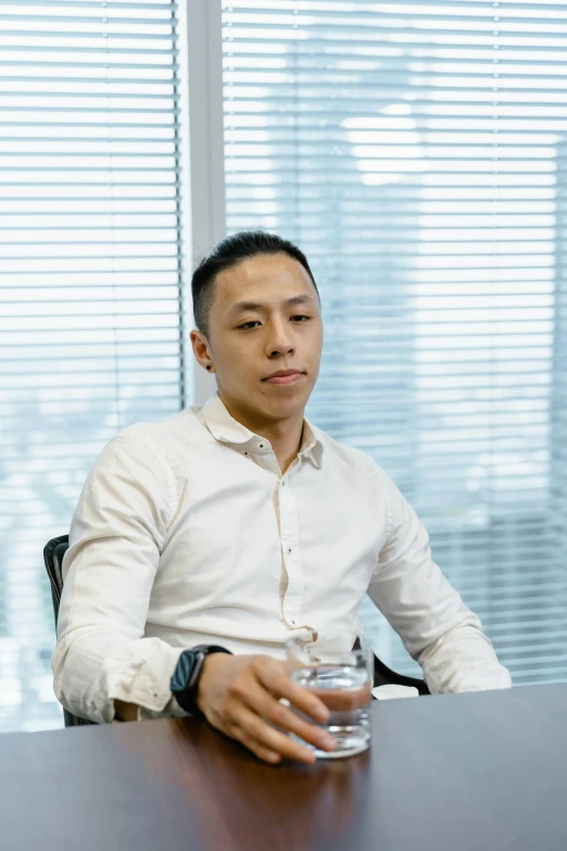 a man sitting at a table with a glass of water, darren quach, in an office, professional profile photo, in tokio