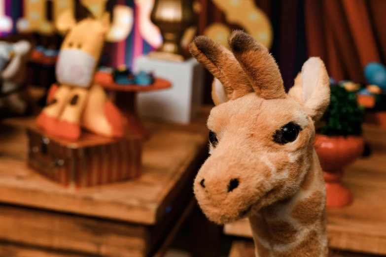 a stuffed giraffe sitting on top of a wooden table, puppets, up-close, toy room, set at night