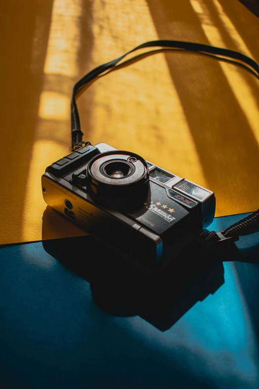 a camera sitting on top of a blue table, a picture, in front of an orange background, looking down on the camera, on a yellow canva, high contrast backlight