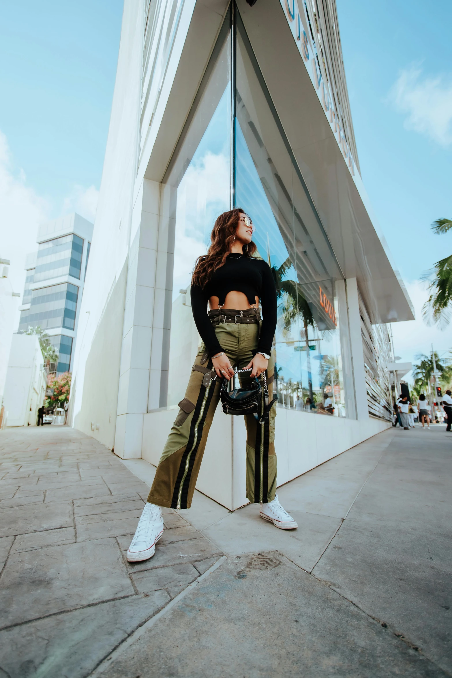 a woman standing in front of a tall building, by Robbie Trevino, military pants, madison beer, miami, official store photo