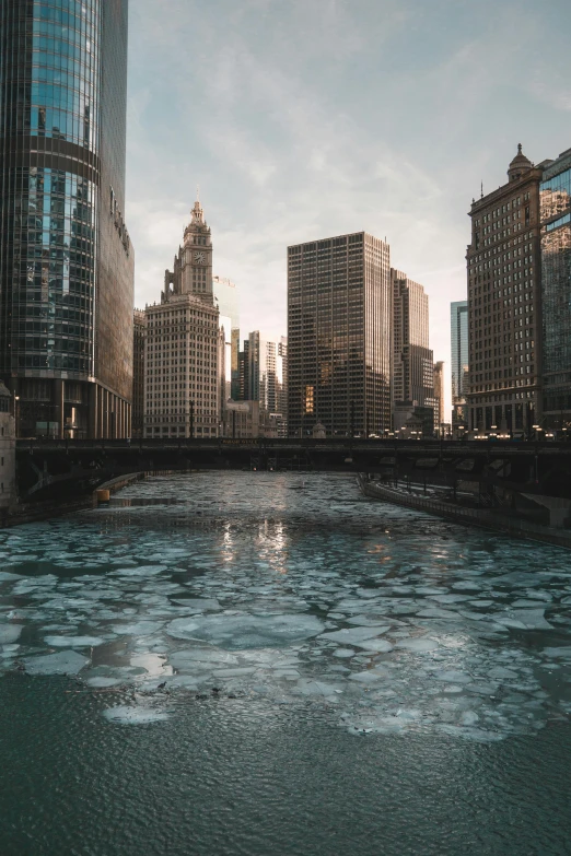 a river running through a city next to tall buildings, by Ryan Pancoast, unsplash contest winner, ice city in 2 0 8 0, from wheaton illinois, bears, erosion