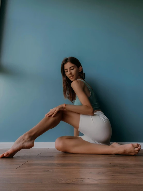 a woman sitting on the floor with her legs crossed, inspired by Elsa Bleda, pexels contest winner, arabesque, smooth tan skin, wearing a tanktop and skirt, standing in corner of room, high arches
