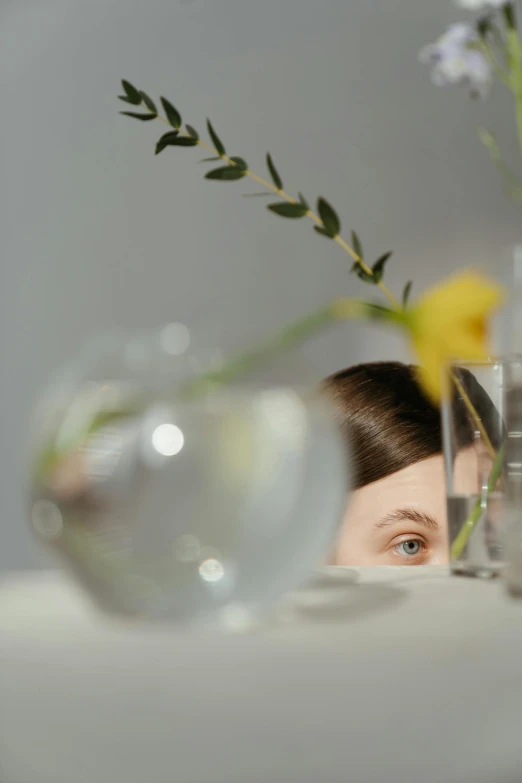 a woman sitting at a table with a vase of flowers in front of her, inspired by Anna Füssli, trending on unsplash, cast glass eyes, fine dining, photographed for reuters, hiding behind obstacles