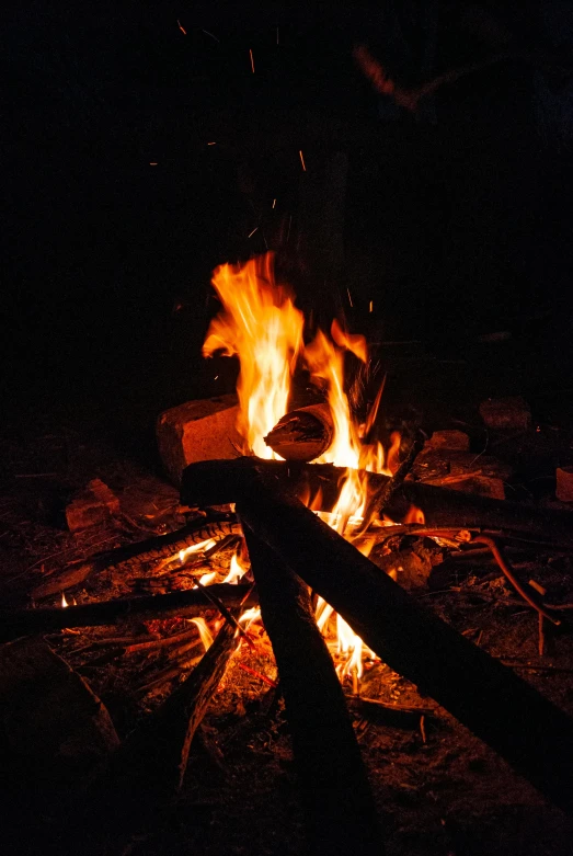 a person standing next to a fire in the dark, pexels, at a campfire at night, smouldering charred timber, arcs of flame, “ iron bark