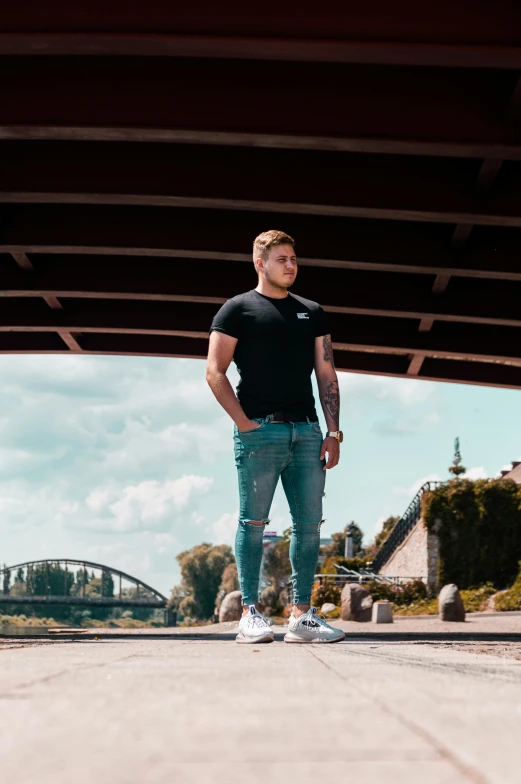 a man standing on a bridge with a skateboard, a picture, by Jacob Toorenvliet, jeans and t shirt, twitch streamer / gamer ludwig, profile picture 1024px, low quality photo