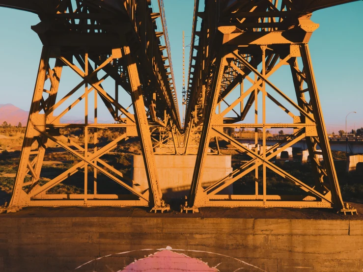 a red fire hydrant sitting under a bridge next to a body of water, an album cover, inspired by Christo, hyperrealism, ochre, symmetrical painting, 1980s photograph, pink golden hour