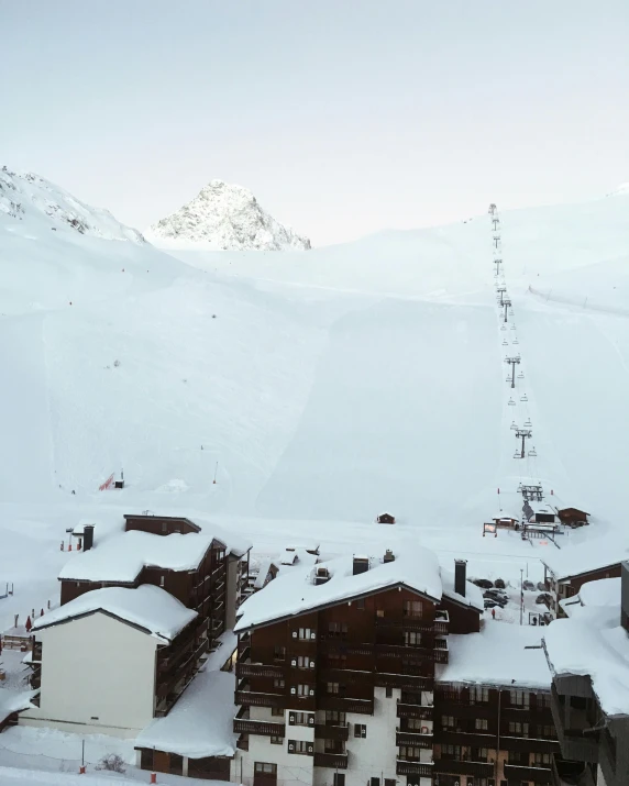 a man standing on top of a snow covered ski slope, lots of building, listing image, seen from above, log cabin beneath the alps