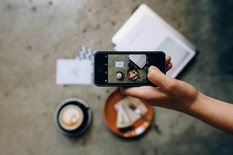 a person taking a picture of a cup of coffee, a picture, unsplash contest winner, mobile learning app prototype, hasselblad photo, on a wooden plate, back facing the camera